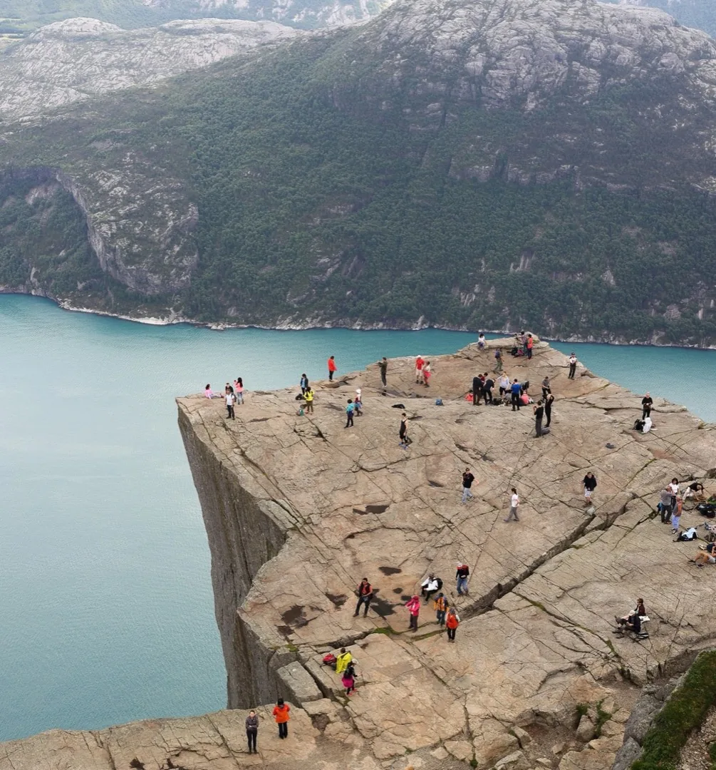Dozens of tourists spread across a flat clifftop high above a fjord